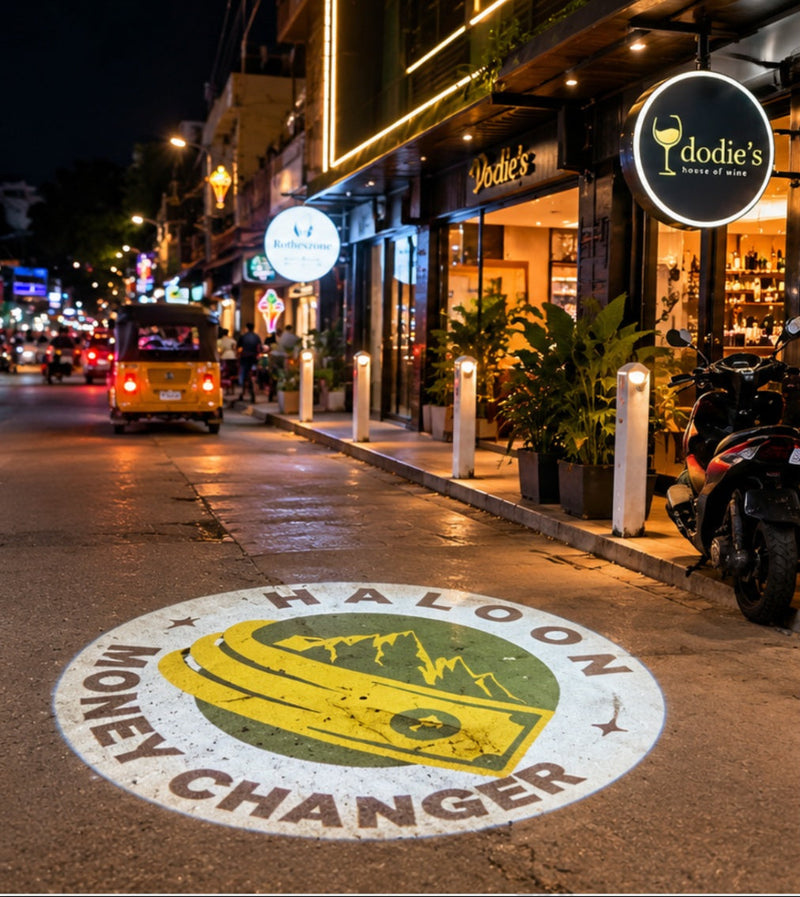 Circular business logo projected onto a street outside shops at night.
